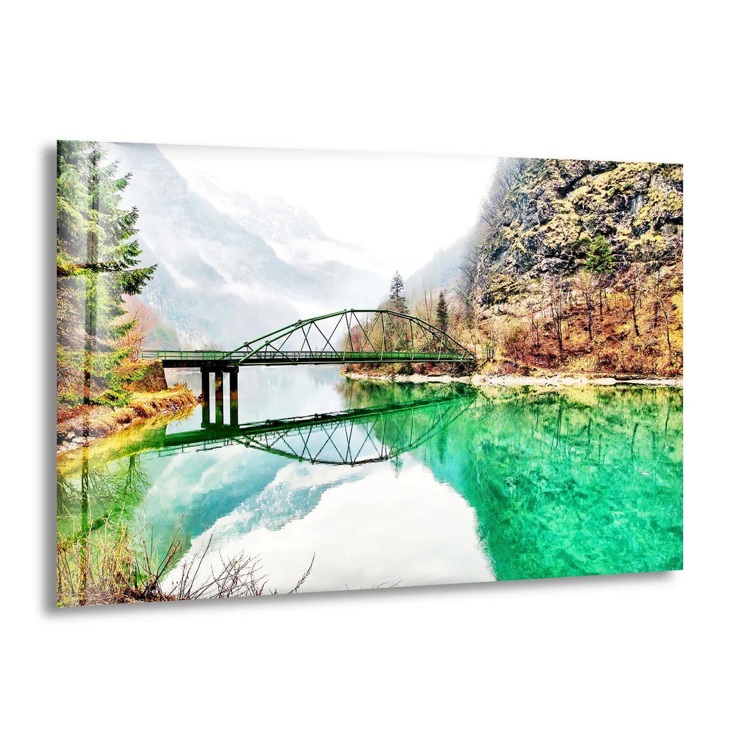 Emerald River Bridge Glass Wall Art featuring a tranquil green river and a scenic mountain backdrop.