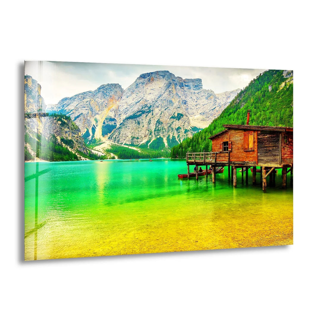 A breathtaking glass wall art featuring a tranquil mountain lake with a rustic wooden cabin.