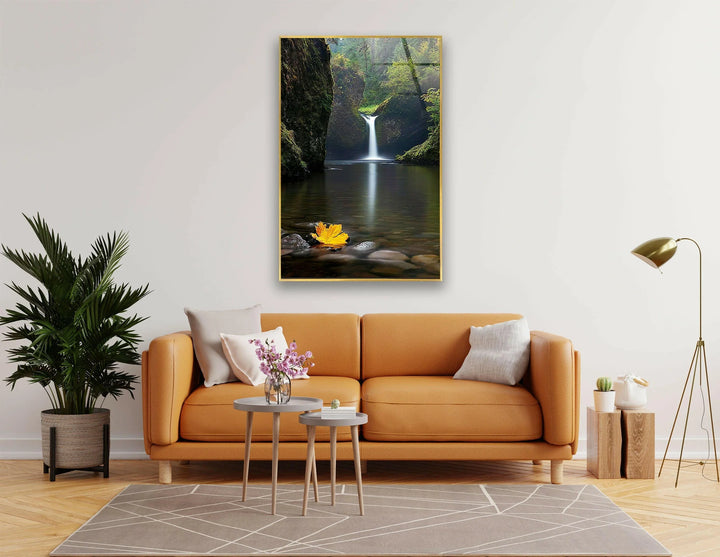 Breathtaking waterfall in a lush green forest with a golden autumn leaf on the water.