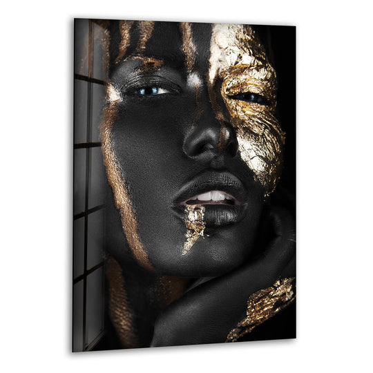 A black background frames this striking glass wall art decor featuring a model's face with black and gold paint.