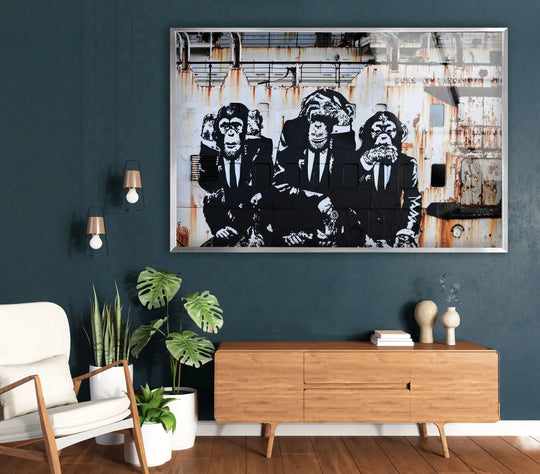Glass wall art of the 3 Monkeys Banksy artwork shows the iconic urban street art in black and white over a wood console