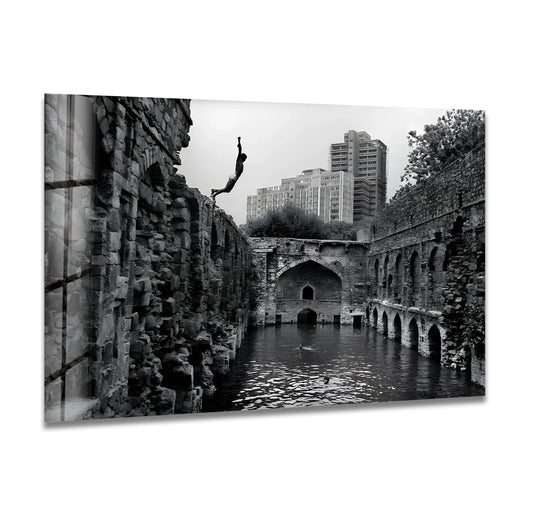 Captured mid-air, the diver is the central subject of this 'Old Delhi Stepwell' art from glass, a striking contrast of historic ruins and modern city buildings.
