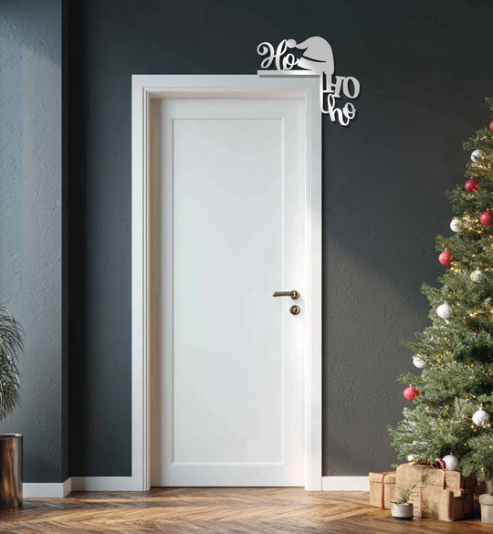 The deepest shadow highlights the stark contrast behind the white door and 'Ho Ho Ho' metal wall decor, a modern metal wall decor bringing festive cheer to a muted space.