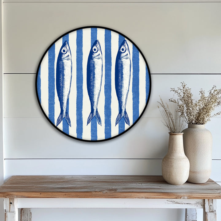 Layers of blue and white stripes create depth in this round canvas wall decor, showcasing a nautical fish illustration for coastal charm.