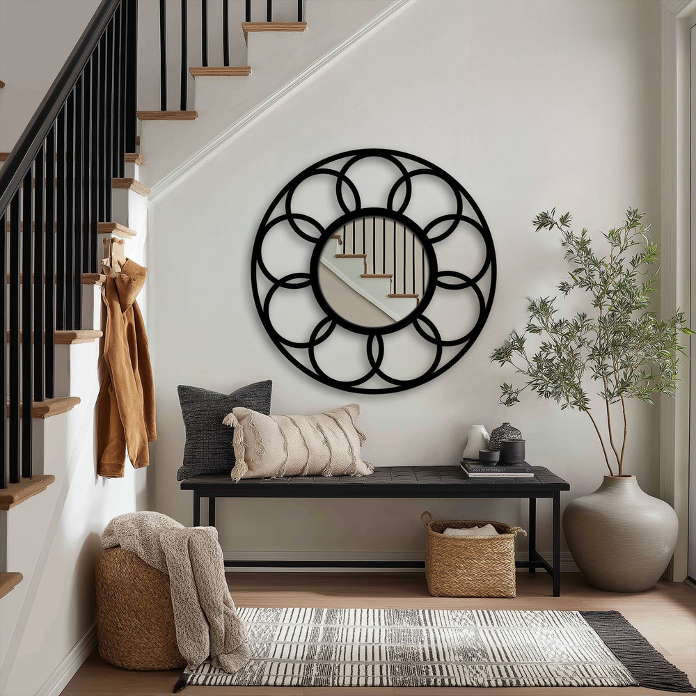 Foreground shows a textured rug leading to a bench with pillows in front of the Harmony Loop interlocking circle black metal floor mirror, enhancing the metal wall decor.