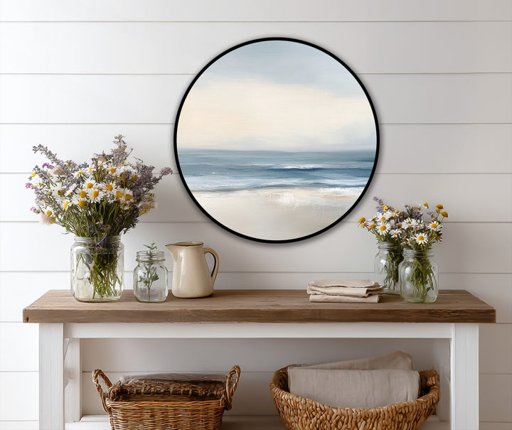 Cool color temperature emanates from the minimalist coastal round oil painting wall art, featuring soft blues in the ocean waves and a calming sky.