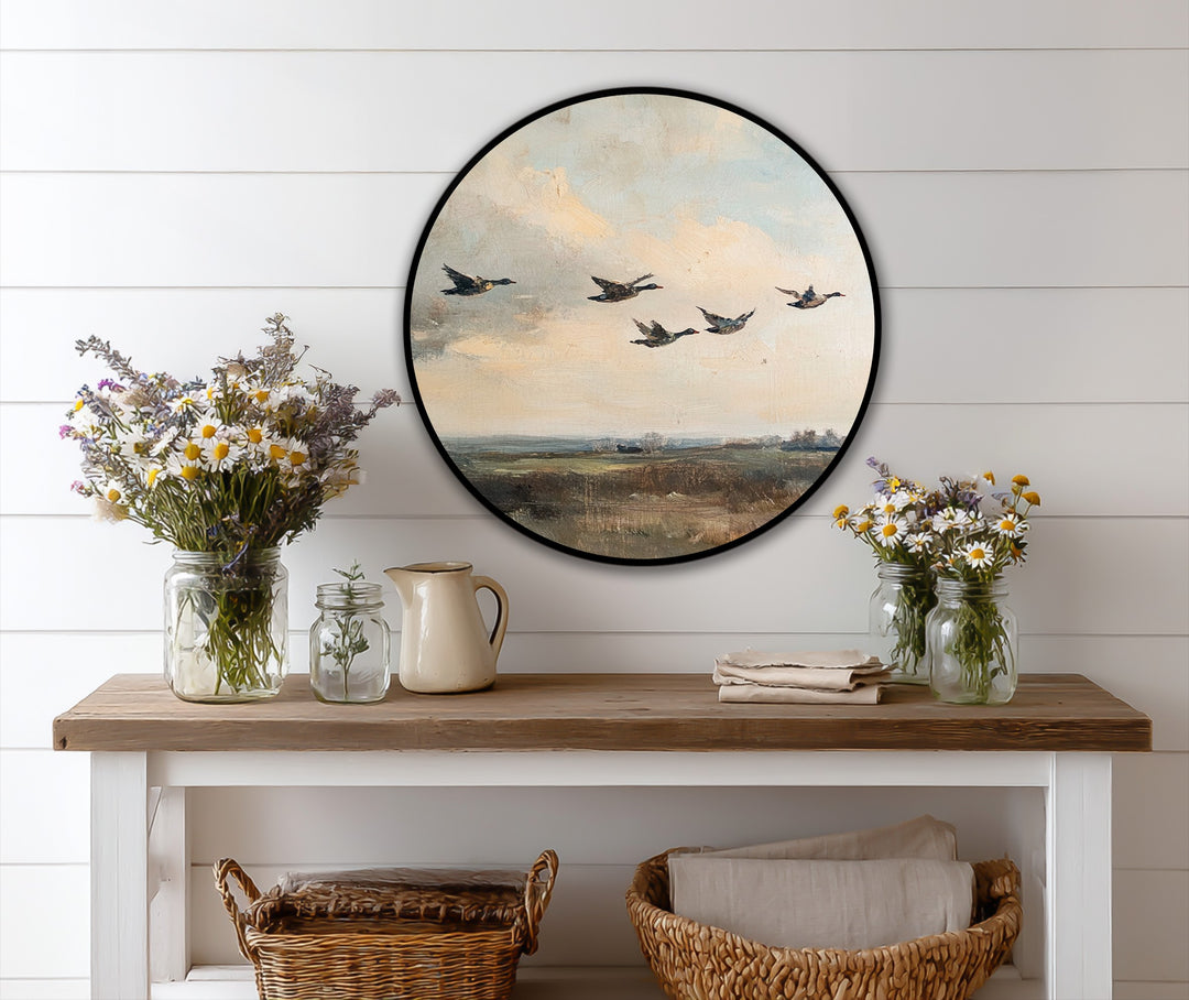 Subtle light and shadow define the vintage flying ducks round oil painting art piece, highlighting the canvas texture and the birds in flight over a shadowed field.