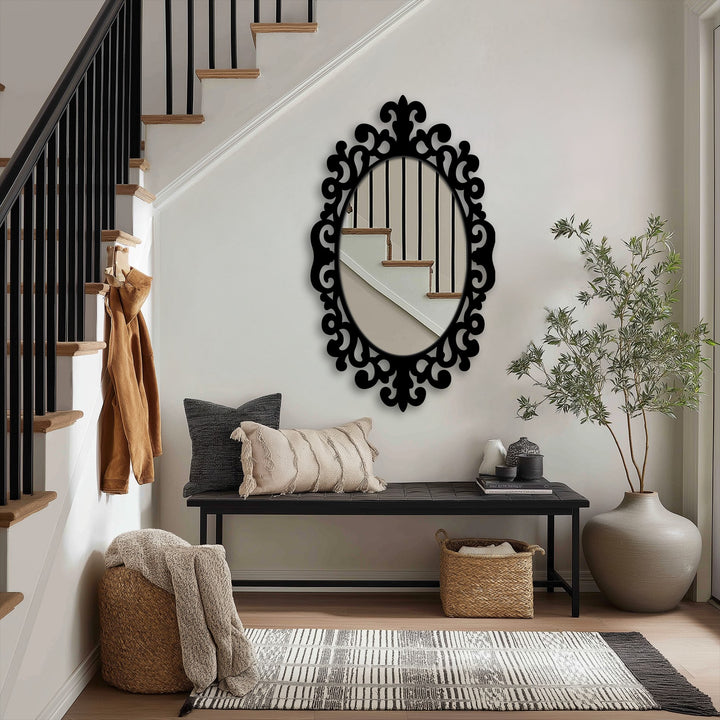 Textured surface of the framed wall mirror showcases an intricate scroll pattern with a smooth oval glass reflecting the nearby stairs and adds depth.