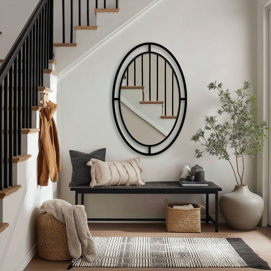 In the foreground, an architectural-style modern oval wall mirror with a segmented frame exemplifies decorating with wall mirrors in a stylish entryway.