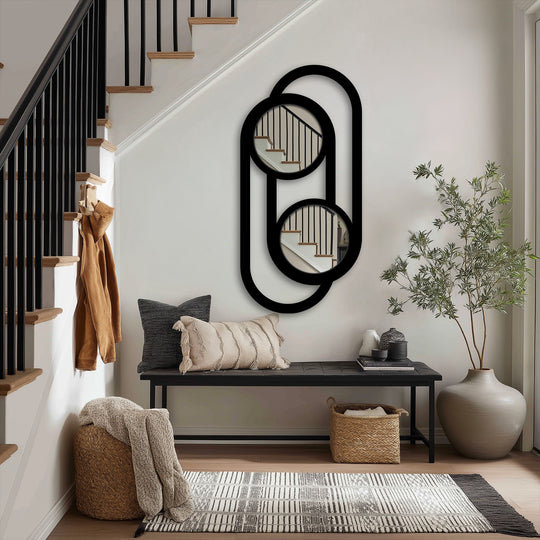 The linked double circle design of this metal artwork forms a modern minimalist wall mirror, reflecting the adjacent staircase and adding an elegant touch.