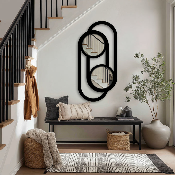 The linked double circle design of this metal artwork forms a modern minimalist wall mirror, reflecting the adjacent staircase and adding an elegant touch.