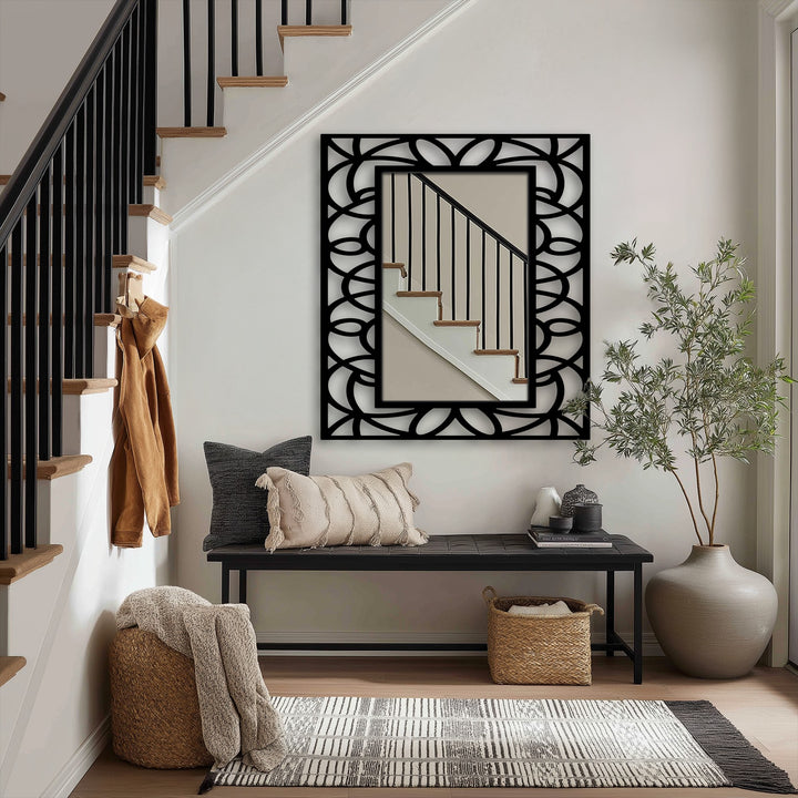 The stillness of the floor mirror's reflection enhances the balanced symmetry of the symmetrical floral geometry frame, a piece of unique metal wall art in black.