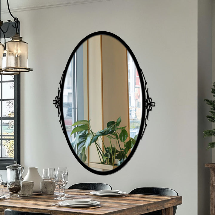 High color contrast highlights the black framed wall mirror against a light wall, reflecting a bright window and indoor plants for an elegant design.