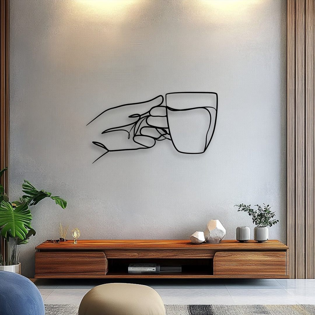 The focal point is a minimalist line art hand holding a cup, serving as a striking unique metal wall art piece on a textured gray wall.