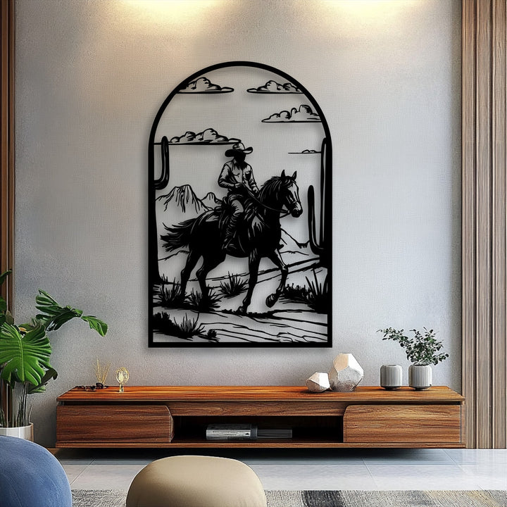 The unique metal wall art features a dramatic arched frame enclosing sharp silhouettes of a cowboy, horse, and desert landscape.