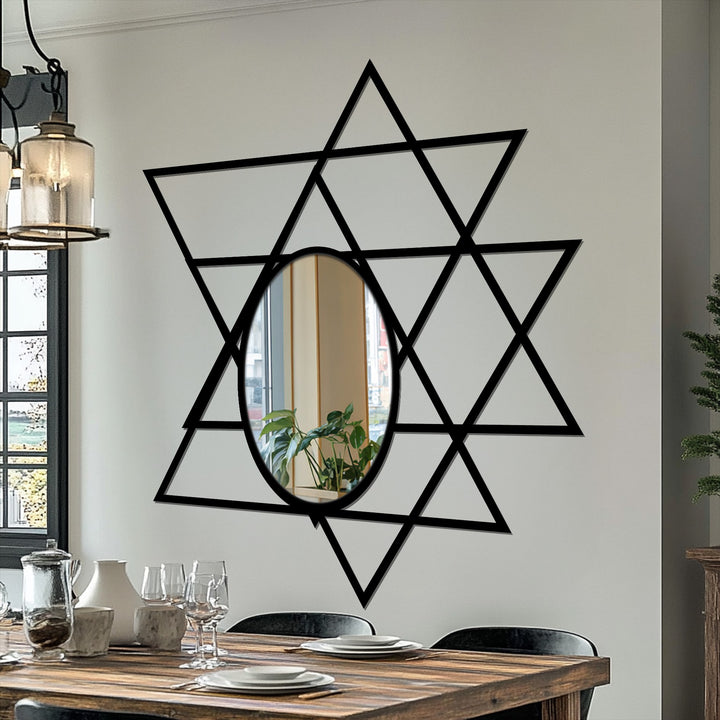 Vertically oriented oval modern mirror reflects a plant within a Star of David formed by black intersecting triangles.