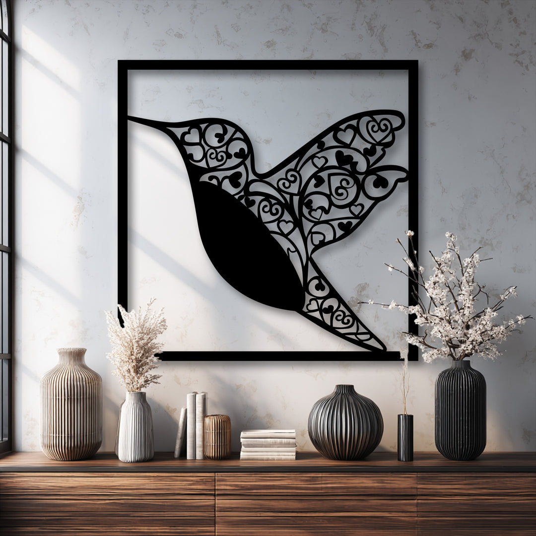 The darkest area, an intricate black hummingbird metal artwork with heart details, is elegantly framed against a light textured wall.