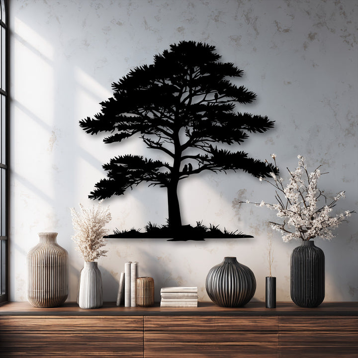 The textured, light gray wall with soft window shadows beautifully frames the intricate tree silhouette metal artwork.