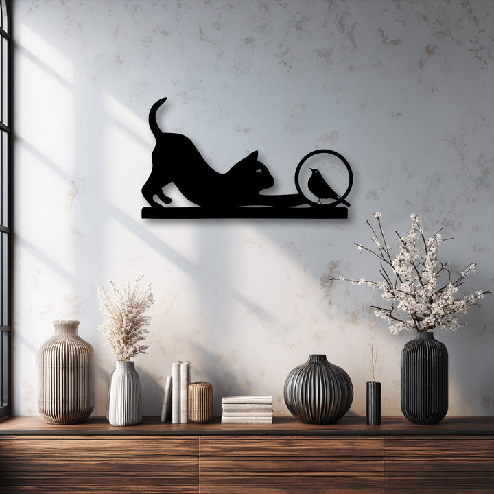 A playful black cat silhouette stretches towards a curious bird perched within a circle, a striking piece of minimalist metal artwork.
