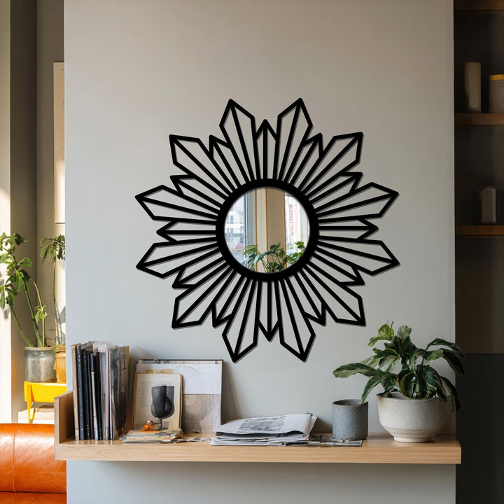 Gray wall provides a neutral backdrop for a sunburst geometric mirror, displaying a shelf with books and plants that add character to the metal artwork.
