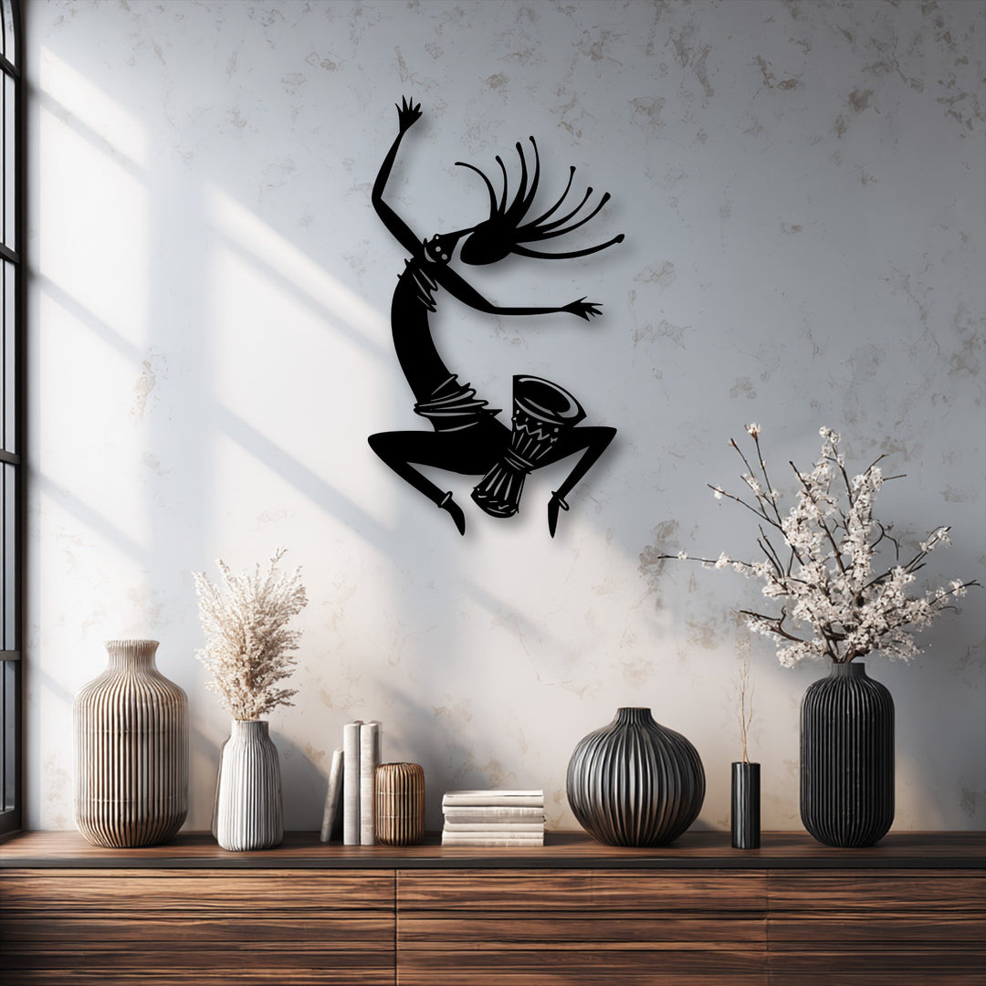 Foreground: a wooden table with ribbed vases and books, beneath the dynamic tribal dance silhouette metal art for wall.