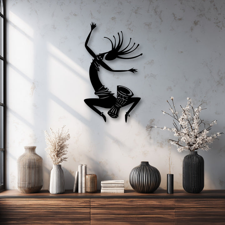 Foreground: a wooden table with ribbed vases and books, beneath the dynamic tribal dance silhouette metal art for wall.