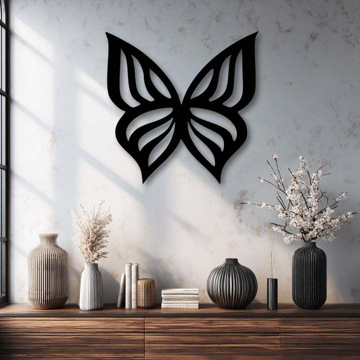 Depth and layers are evident in the butterfly metal artwork casting its shadow on the wall above vases and books on a wooden shelf.