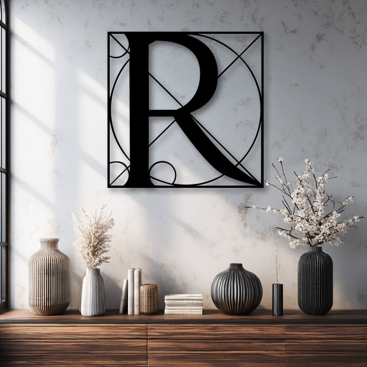 A warm-toned decorative metal art piece featuring a geometric letter R wall hanging casts soft shadows on a sunlit, textured wall.
