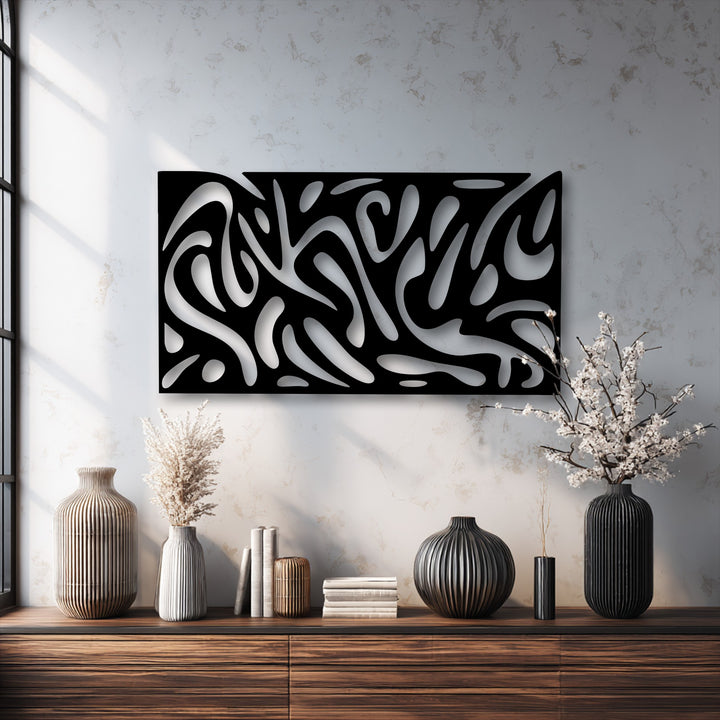 The distinctive surface texture of the abstract fluid pattern metal art for wall features smooth black and glossy silver cutouts on a mottled wall.