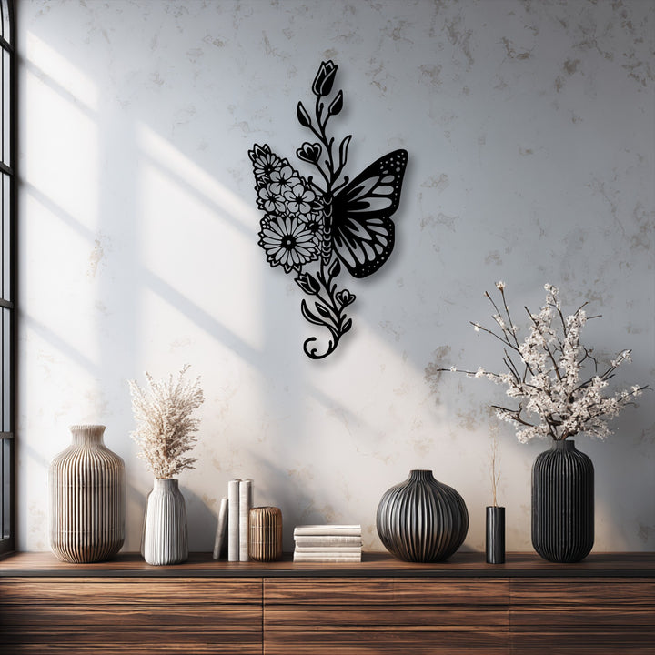 The vertical, elongated metal artwork showcases an elegant butterfly shape with one wing formed by intricate floral and botanical elements.