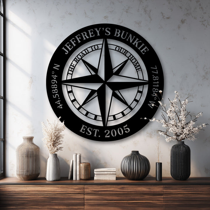 A striking black personalized compass metal artwork creates a clean aesthetic against a bright, textured light gray wall.