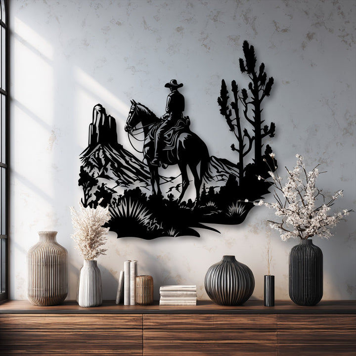 The sunlit bright white wall highlights the striking black silhouette of this unique metal wall art, showing a cowboy on horseback in a desert scene.