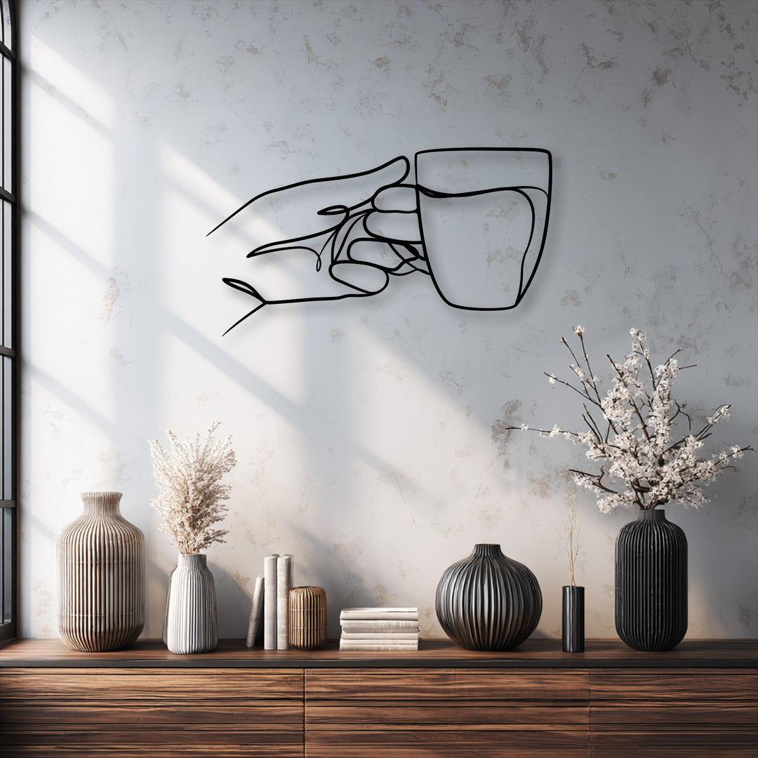 The bold color contrast of this decorative metal art showcases a minimalist black line drawing of a hand holding a cup against a light, textured wall.