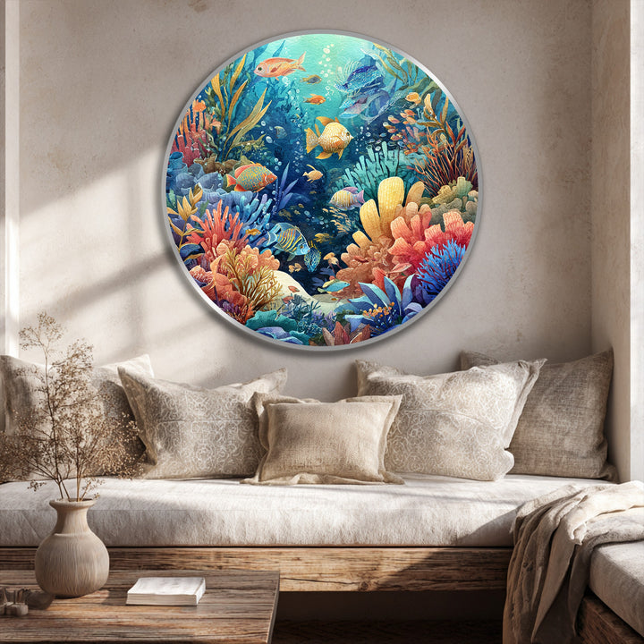Foreground shows a vase and book on a wooden table, enhancing the scene with vibrant coral reef round oil painting wall art hanging above the cushions.