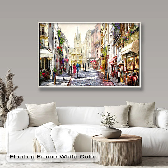 A framed wall art featuring a charming European street with cobblestone paths, elegant cafés, and historic architecture, illuminated by soft daylight
