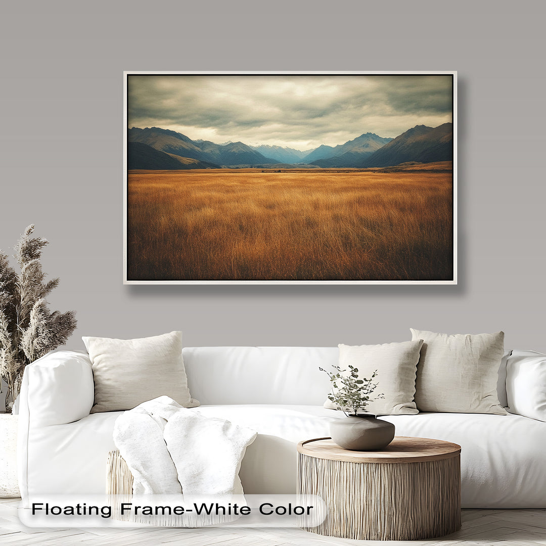 Golden prairie painting with majestic mountain backdrop and cloudy sky.
