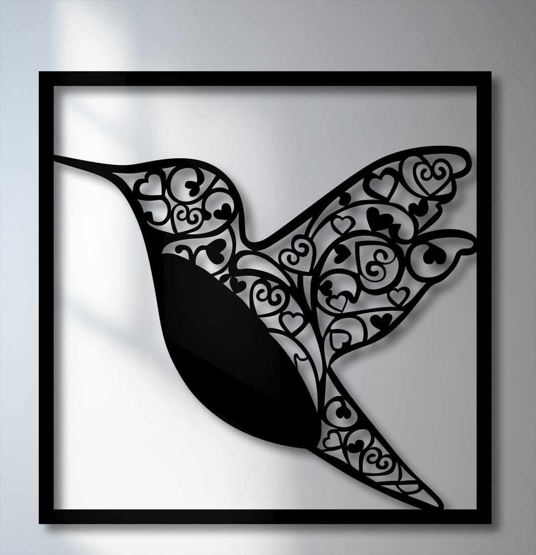 The matte black finish of the intricate hummingbird metal artwork casts elegant shadows, highlighting the delicate heart and swirl cut-outs.