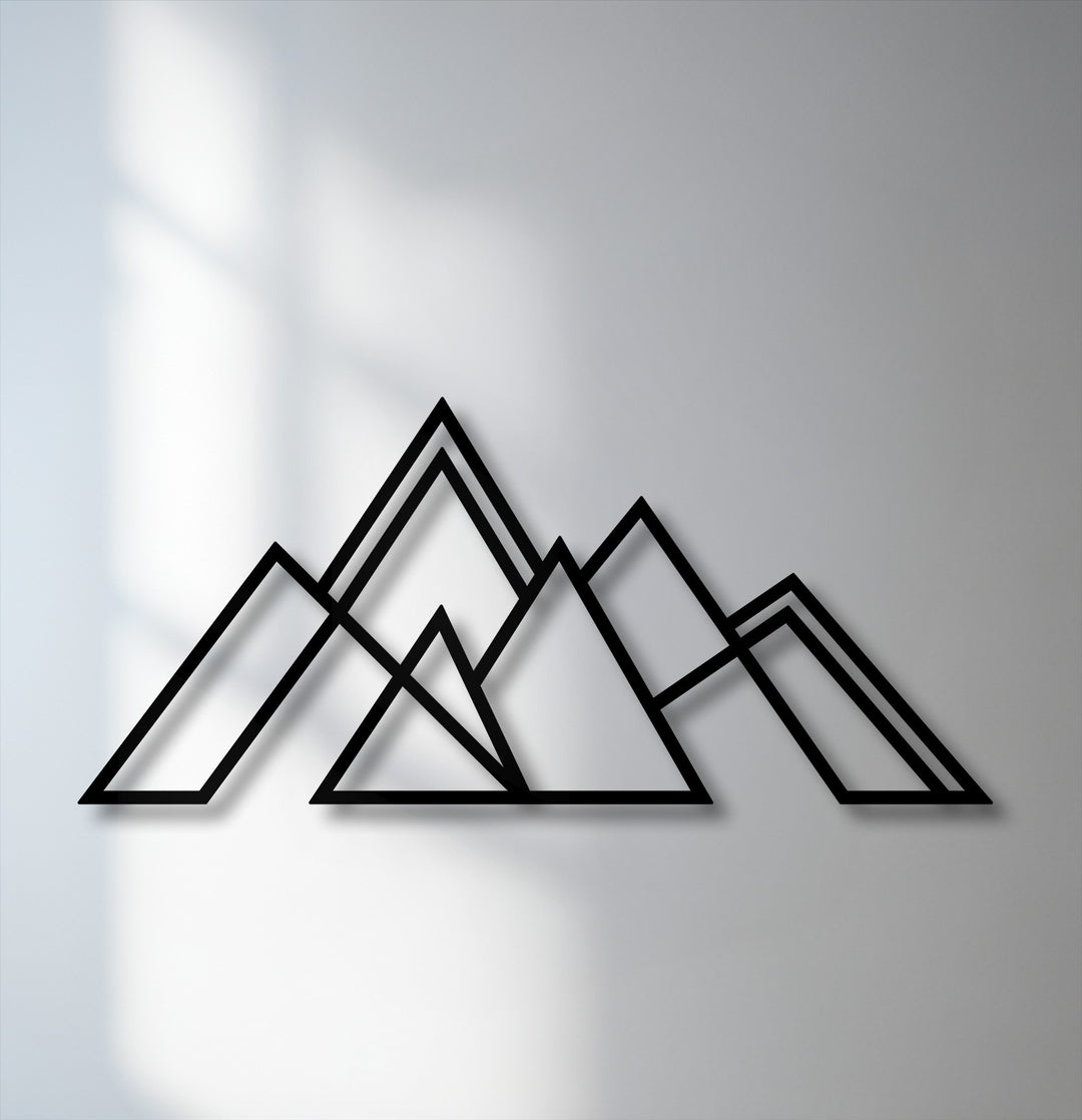 The smooth, matte finish of the geometric mountain metal wall decor contrasts with the subtle texture of the light grey wall.