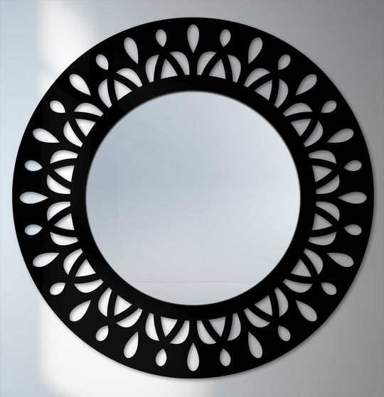 Foreground detail showcases the leaf motif in decorative metal art, forming a modern black statement frame around the round floor mirror.