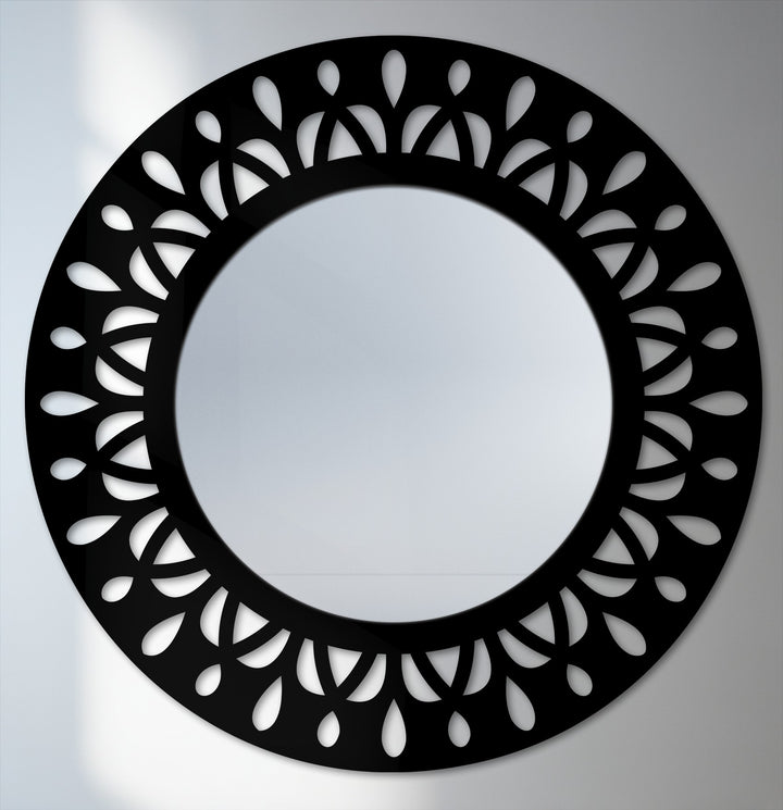 Foreground detail showcases the leaf motif in decorative metal art, forming a modern black statement frame around the round floor mirror.