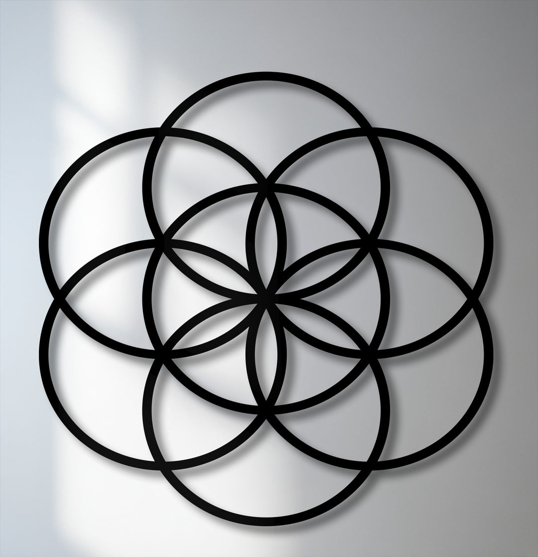 The organic forms of the black Flower of Life geometric metal artwork elegantly intersect, casting soft shadows on a light wall.