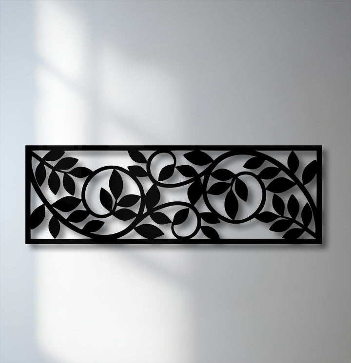 The intricate black metal artwork panel features a flowing botanical vine pattern with stylized leaves, casting elegant shadows on the wall.