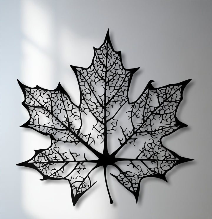 The cool color temperature highlights the intricate maple leaf silhouette metal wall decor, casting crisp shadows on a light background.