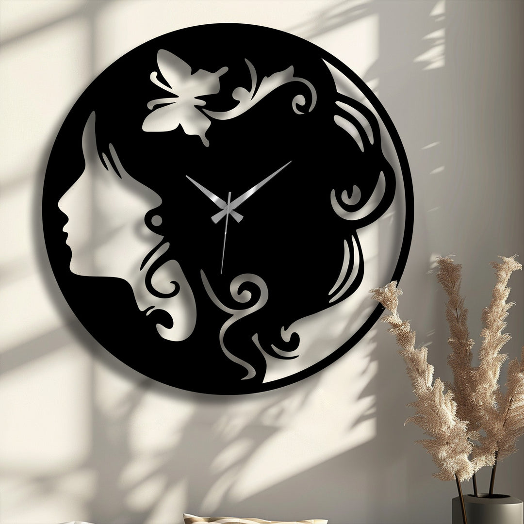 An elegant black metal wall decor clock displays a woman's silhouette with flowing hair and a delicate butterfly accent, featuring silver hands.
