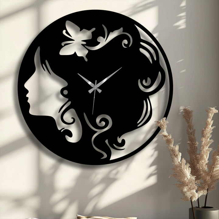 An elegant black metal wall decor clock displays a woman's silhouette with flowing hair and a delicate butterfly accent, featuring silver hands.