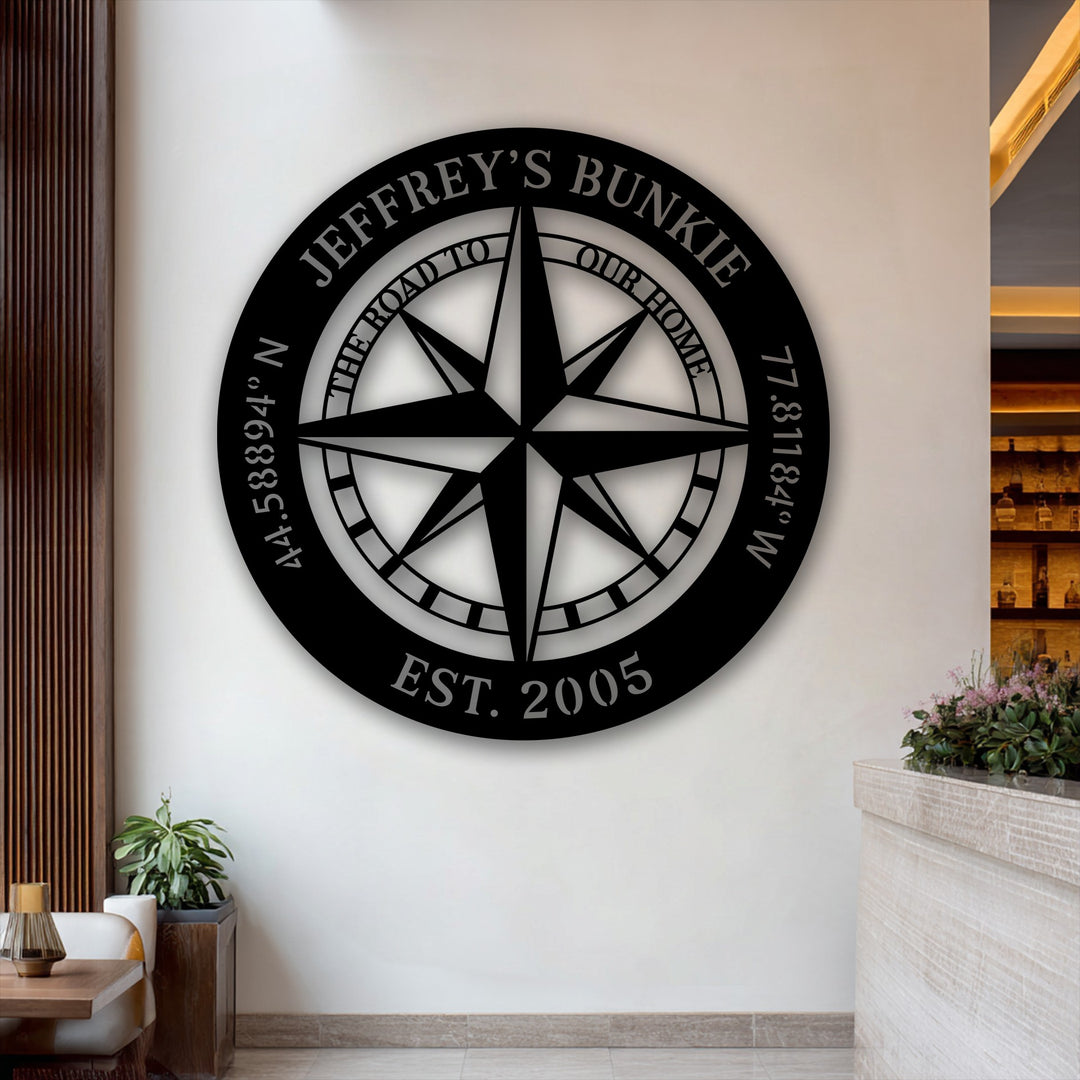 The bold custom name compass metal art for wall displays a sharp transition from its deep black finish to the bright white wall, with subtle shadow gradients.