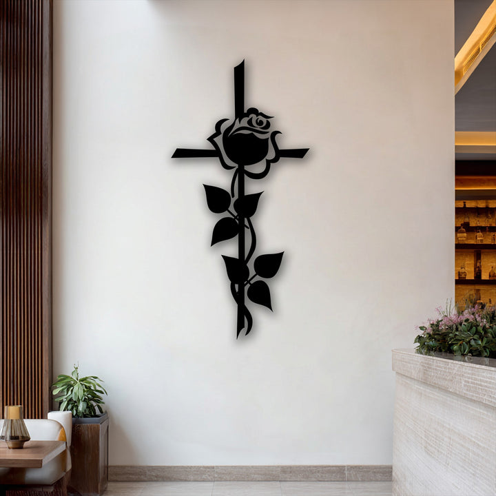 The matte black finish of this unique metal wall art showcases a striking rose cross silhouette, casting a subtle shadow on the white wall.