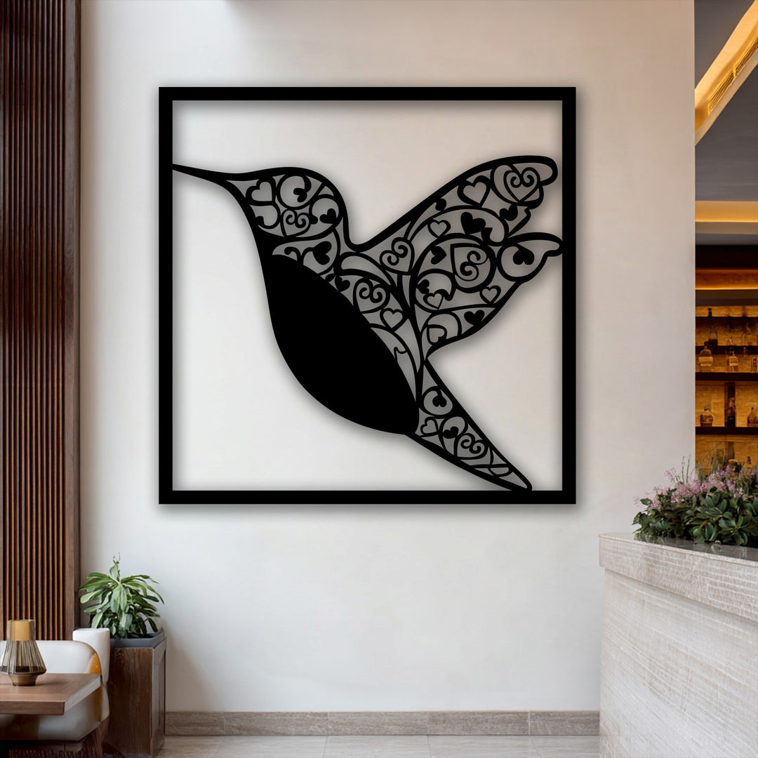 The striking transition from the dark, intricate hummingbird heart metal wall decor to the bright white wall highlights the artwork's design.