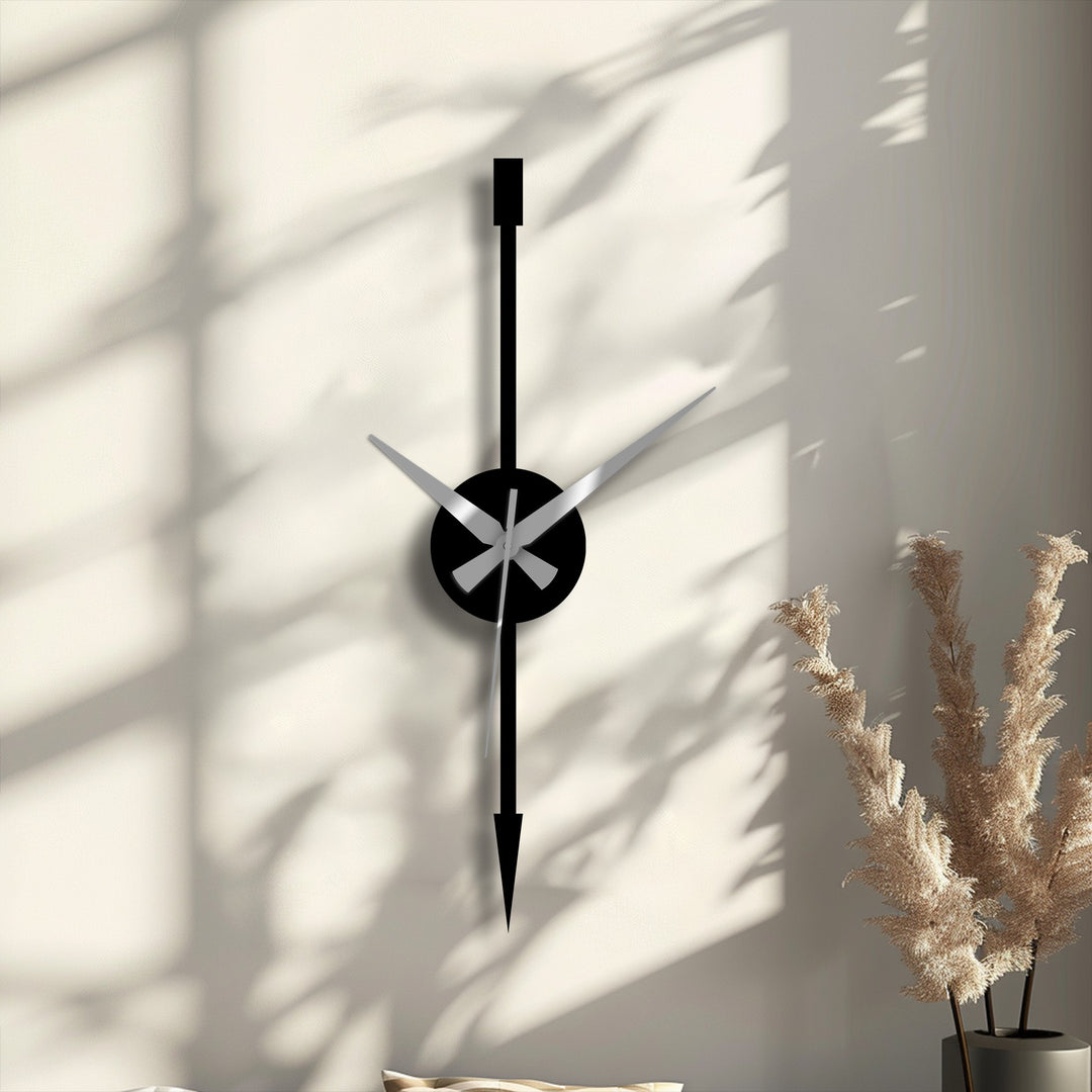 Shadowed against the neutral wall, the bold, black clock face and hands of this minimalist vertical arrow metal artwork create a striking contrast.