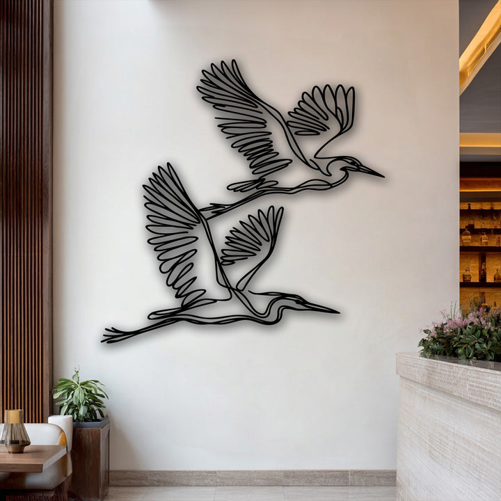 Delicate pink blossoms gently adorn the light counter, beautifully contrasting the graceful herons minimalist metal decoration wall art.